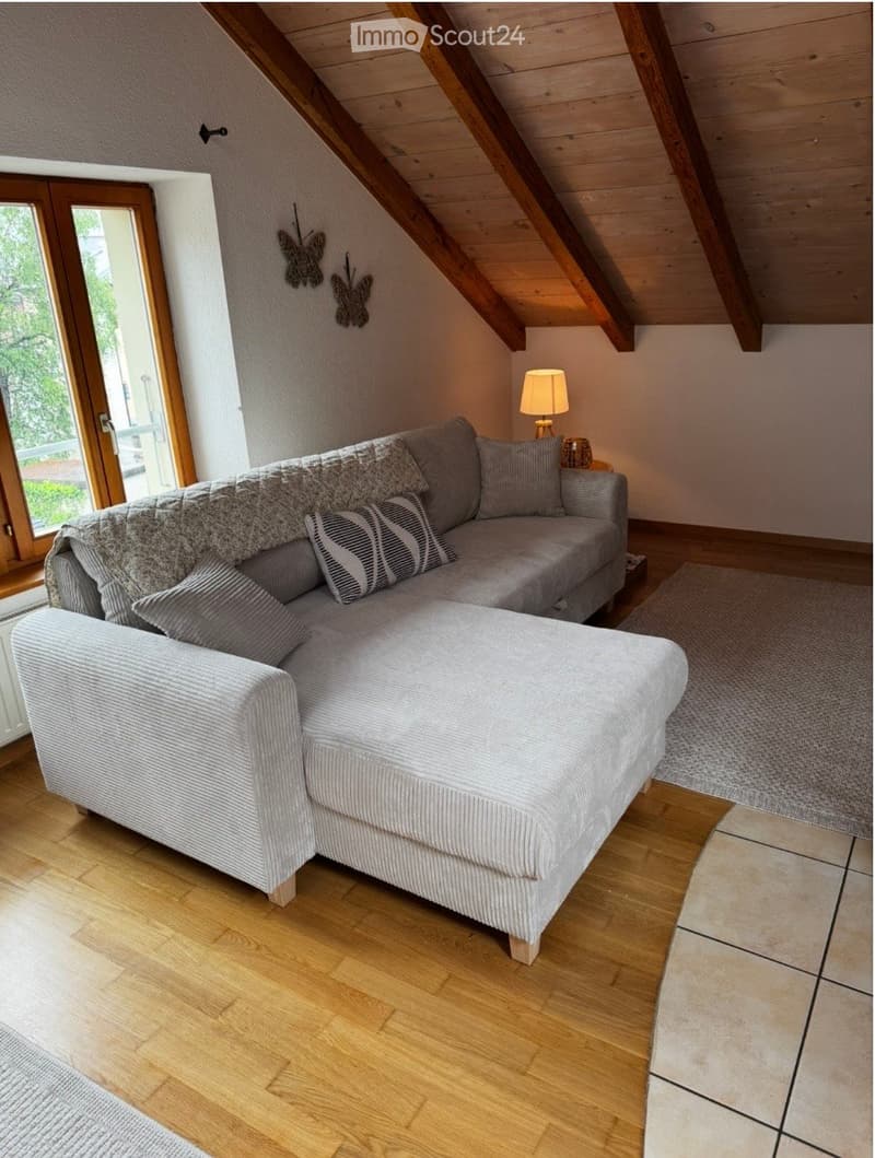 Cozy living room with a grey sectional sofa, ottoman, table lamp, and decorative rug on wooden flooring.