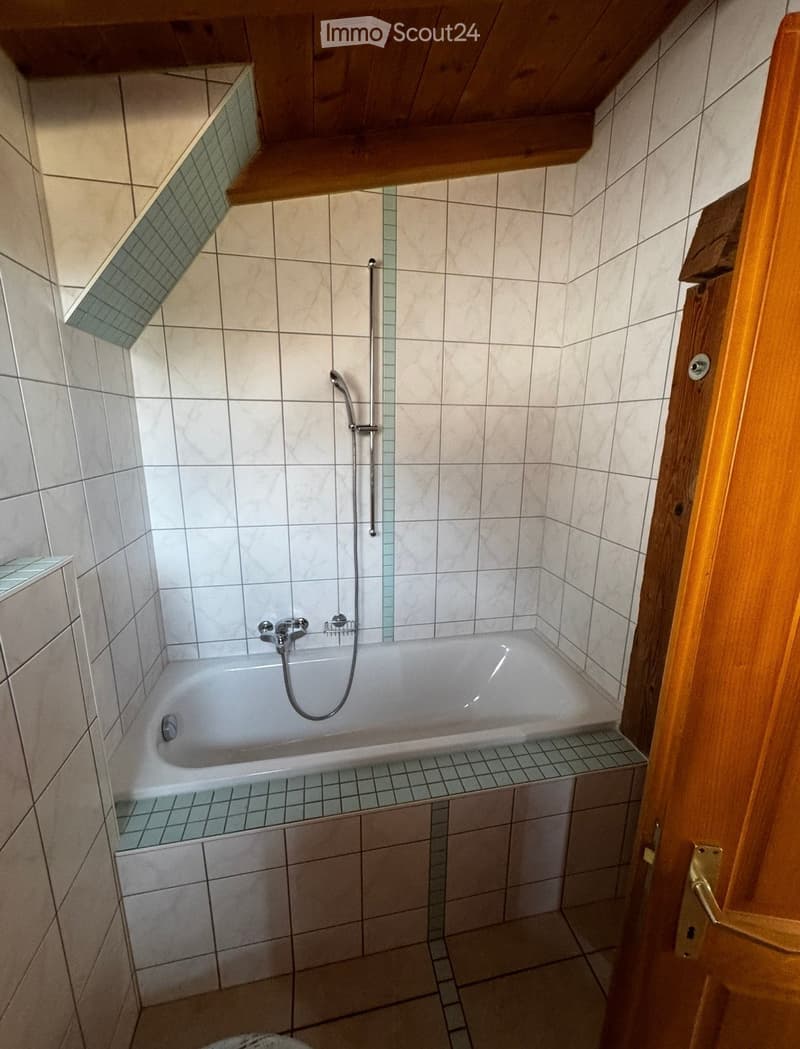Small bathroom with a bathtub, tiled walls, and a wooden door frame.