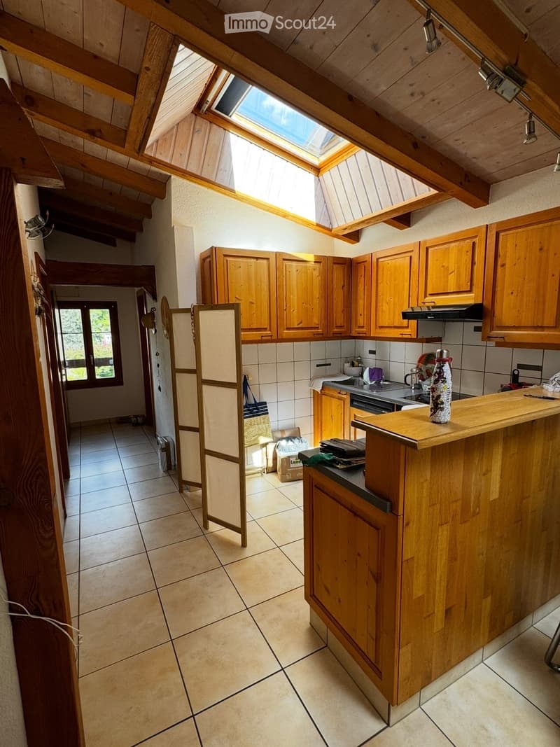 Bright kitchen with wooden cabinets, a central island, and a skylight above. The space includes a sink, oven, and various kitchen items on the counter.