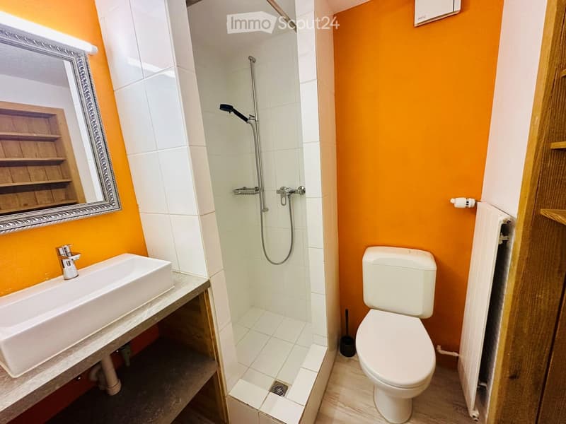 Bathroom with a white sink, mirror, toilet, and shower area. The walls are painted in bright orange and white tiles.