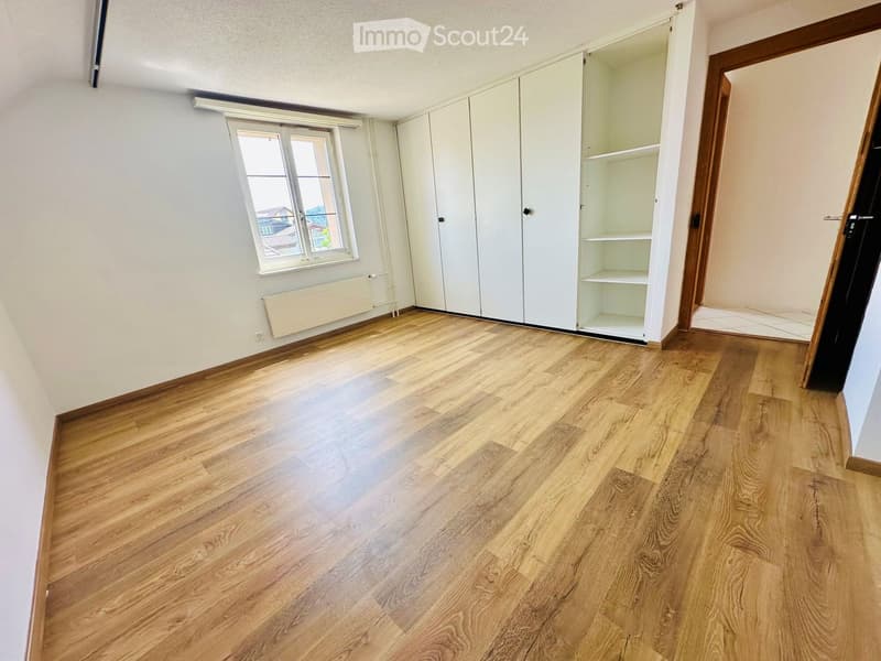 Empty room with wooden flooring, white walls, built-in closet with open shelves, and a window with white frame.