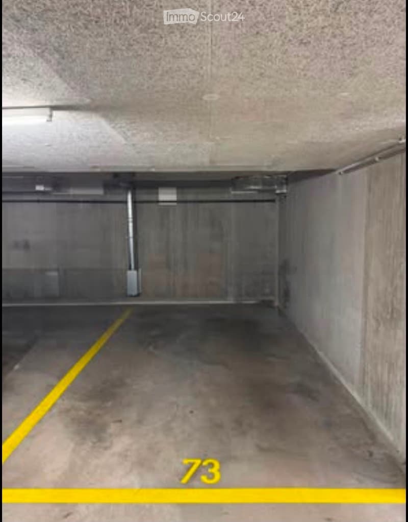 Empty underground parking space with concrete walls and ceiling, marked parking spots, and a visible number '73'.