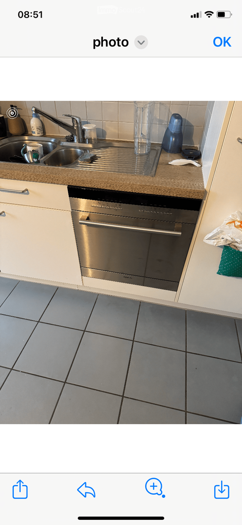 Modern kitchen with a stainless steel dishwasher, sink, and various cups and bottles on the counter.