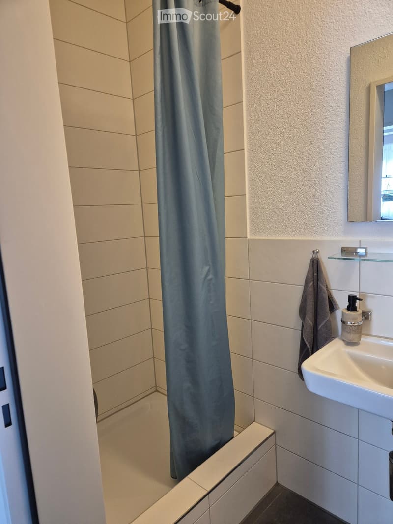 Modern bathroom with a white sink, mirror, towel, and shower curtain. The walls are tiled in light beige and white.