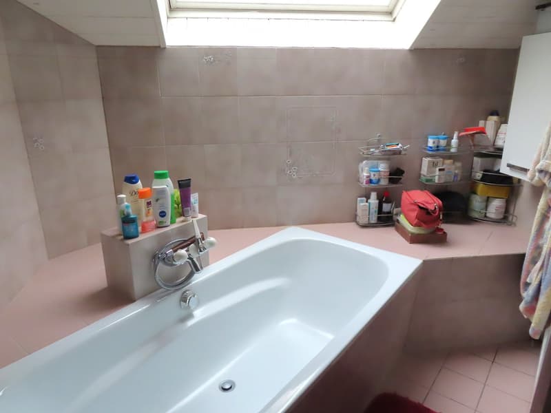 Bathroom with a white bathtub, tiled walls, and shelves holding various toiletries and cosmetics.