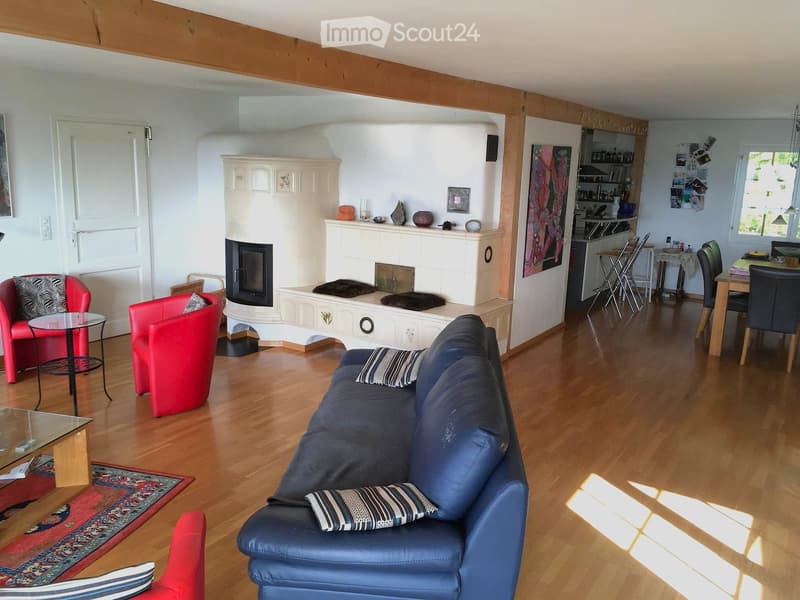 Living room with wooden flooring, fireplace, blue sofa, red armchairs, coffee table, and dining area with chairs and table.
