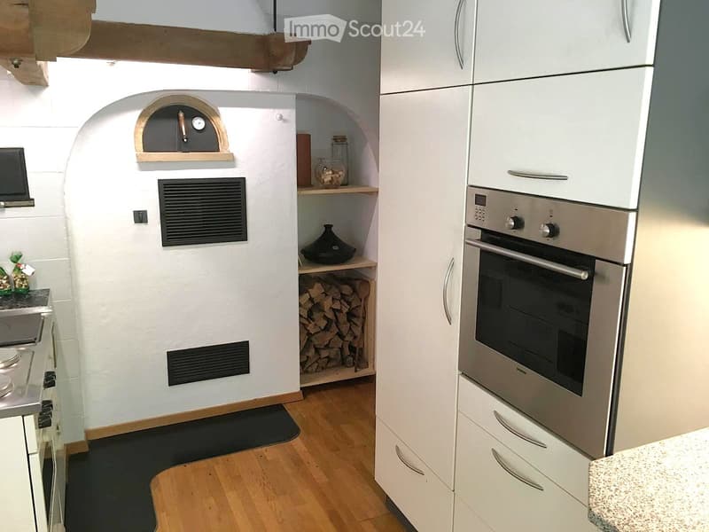 Modern kitchen with white cabinets, stainless steel oven, wooden floor, and wooden shelves holding firewood and decorative items.