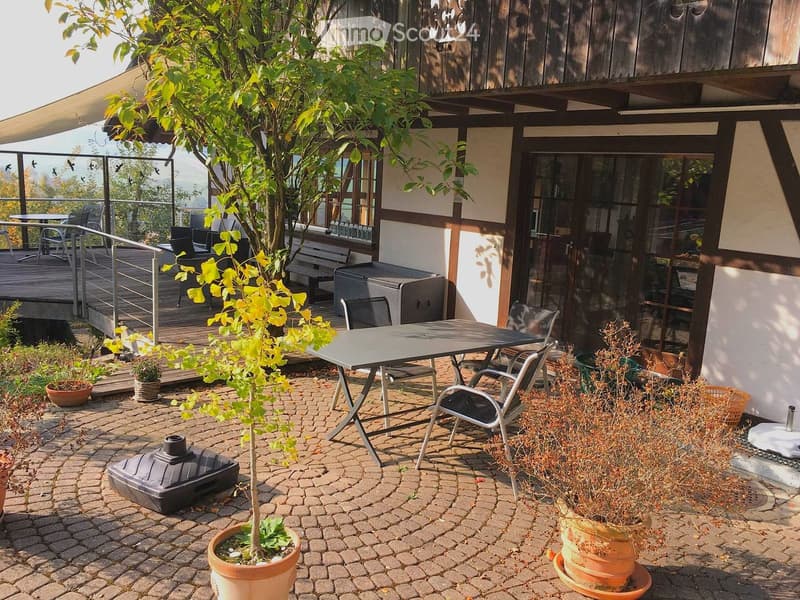 Garden area with a small table and chairs, potted plants, and a view of a wooden deck and building.