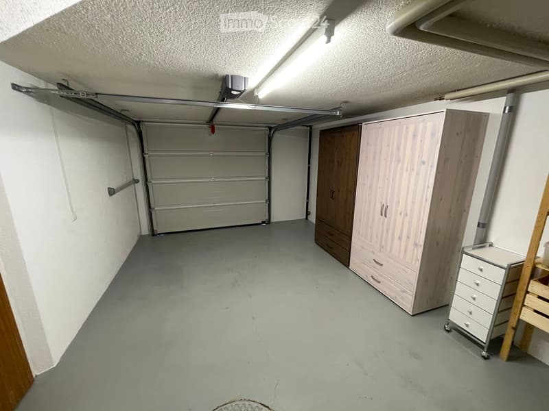 Empty garage with a closed garage door, storage cabinets, and a small rolling cart.