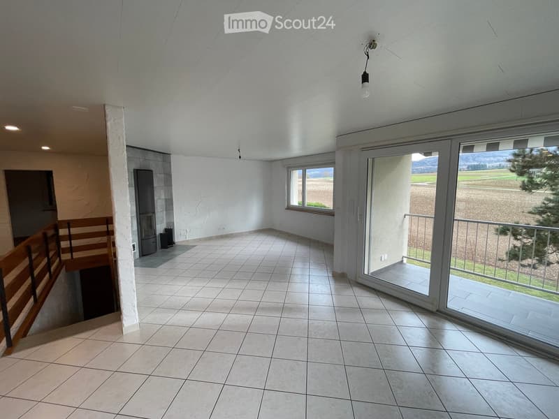 Empty room with tiled floor, white walls, large windows, and a sliding glass door leading to a balcony with a view of a field.