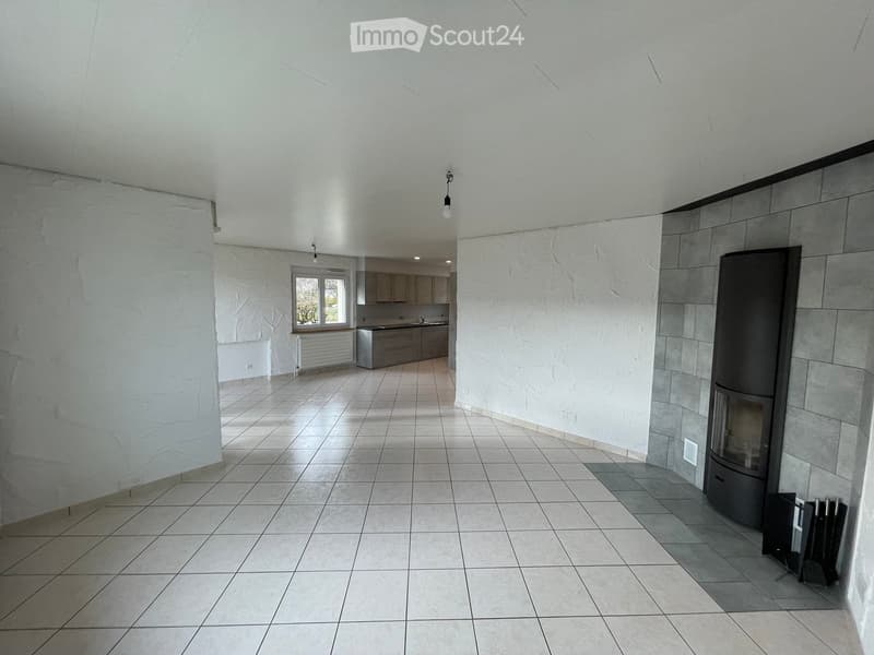 Open-plan living and dining area with a modern fireplace, tiled flooring, and a visible kitchen area with cabinets and a sink.
