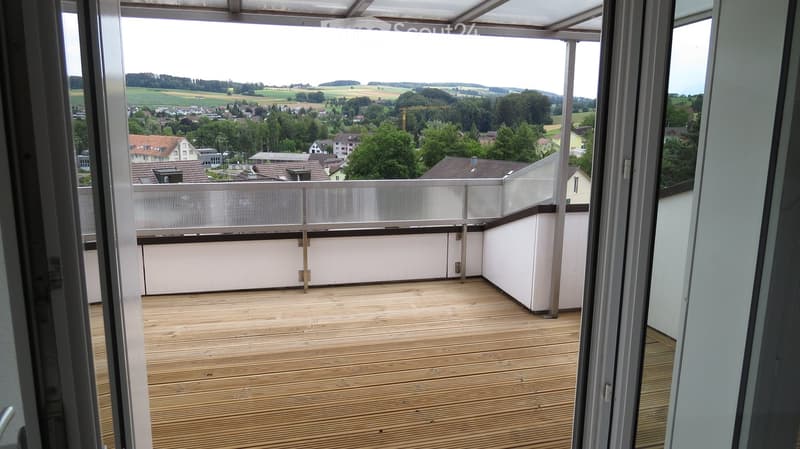 Balcony with wooden floor, metal railing, open sliding doors, view of the town
