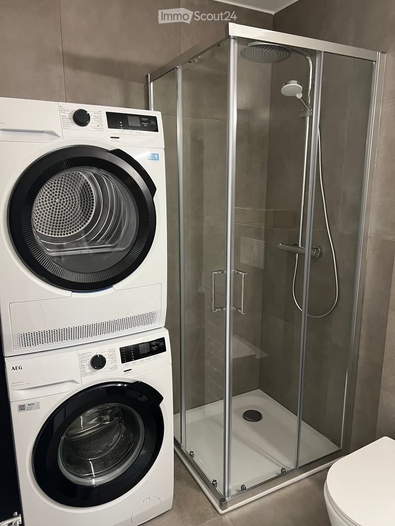 Modern bathroom with a glass-enclosed shower, a washing machine, and a toilet.