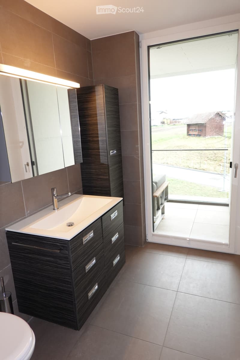 Modern bathroom with dark wood cabinetry, a white sink, a mirror, and a large window offering a view of the outdoor area.