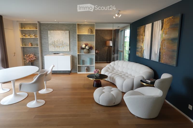 Modern living room with a white sofa, white chairs, a white dining table, a black coffee table, and decorative shelves with vases and artwork.