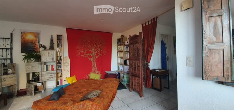 Cozy bedroom with a large bed covered in orange and blue bedding, surrounded by bookshelves, a small table, and a red curtain with a tree design.