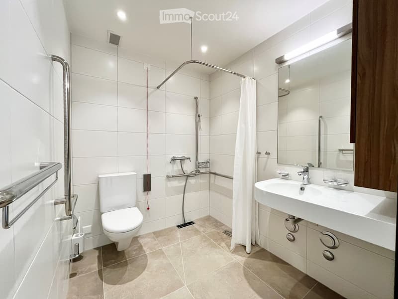 Modern white bathroom with a walk-in shower, toilet, sink, and various fixtures; spacious and bright