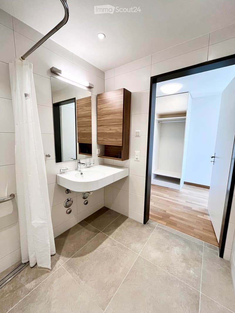 white wall, wooden floor, large mirror, sink, wooden cabinet, light fixtures, white wardrobe, open door