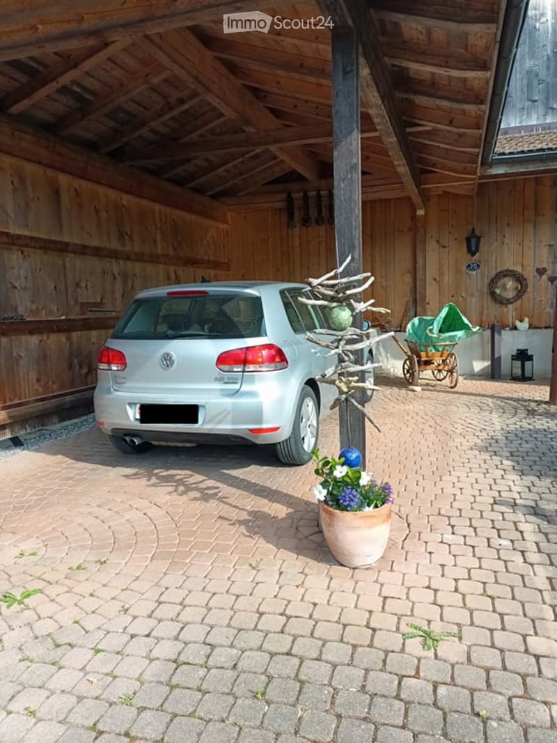 Garage with wooden beams and a parked car, featuring a potted plant and a decorative cart nearby.