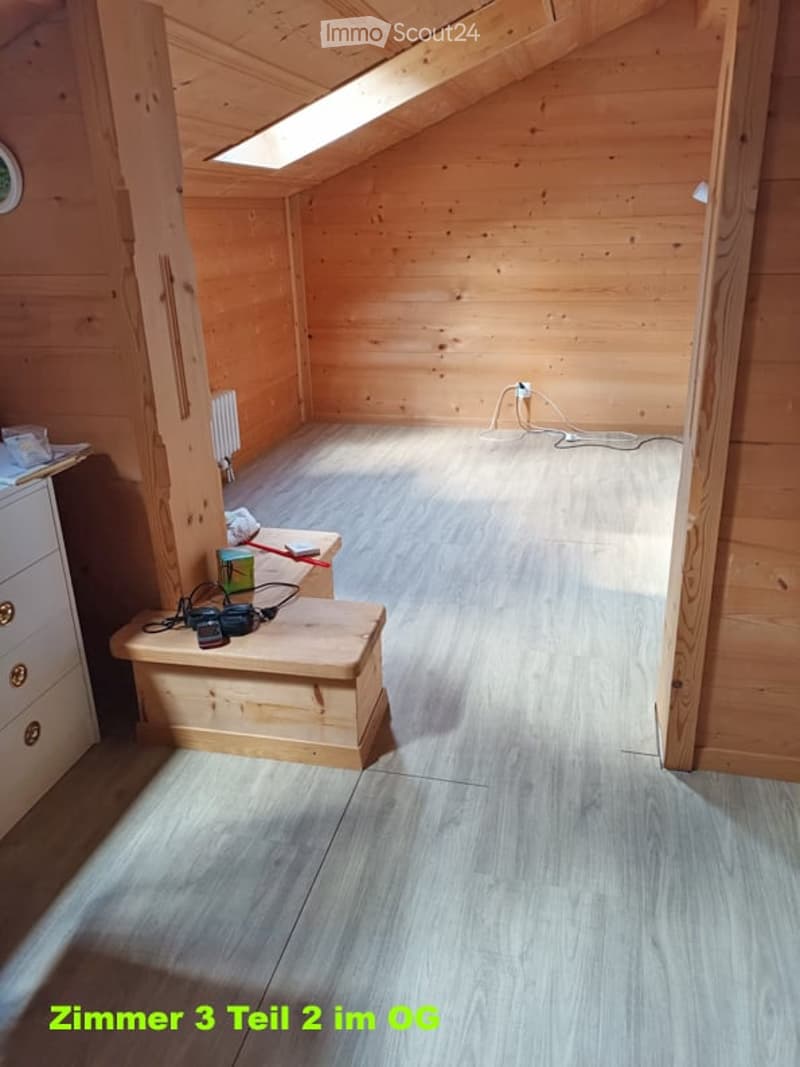 Wooden attic room with slanted ceilings, light wooden walls, and a small wooden stool holding tools and a drill. A radiator is visible on one wall.