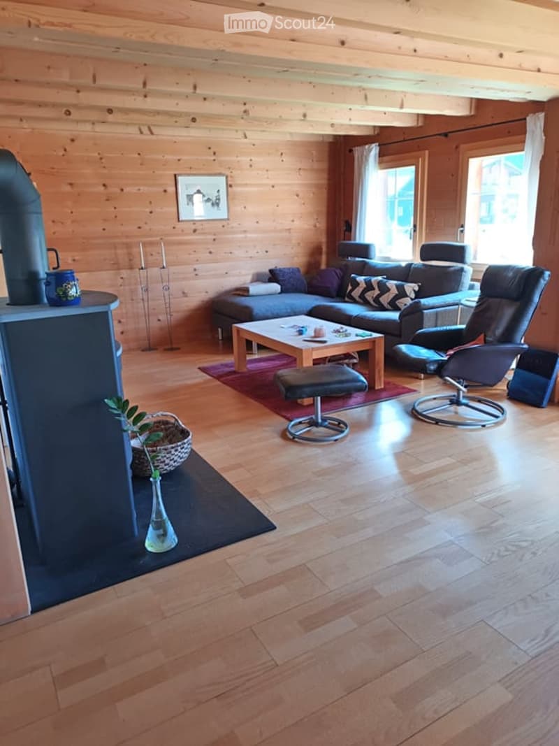 Cozy living room with wooden walls and floors, a grey sectional sofa, coffee table, ottoman, and a fireplace with a vase and basket nearby.