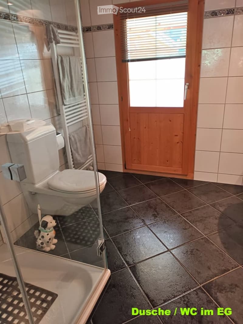 Bathroom with a toilet, glass-enclosed shower, towel rack with towels, and a small toy dog on the floor.