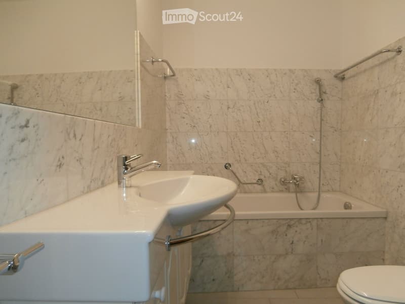 Modern bathroom with marble tiles, double sink, bathtub, and toilet.