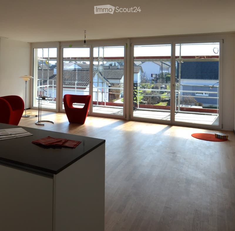 Furnished Room. Bright room with large windows and a view of the neighborhood, featuring a red chair, a small table, and a floor lamp.