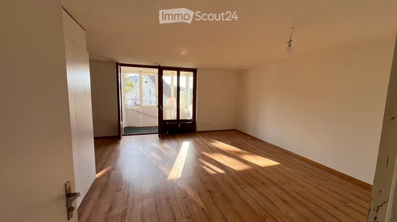 Empty room with wooden flooring, white walls, and a large window with a view of the outside. The room is unfurnished and has a simple, clean design.