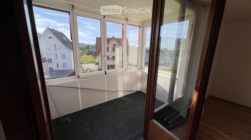 Empty room with large windows offering a view of the neighborhood, carpeted floor, and white walls.