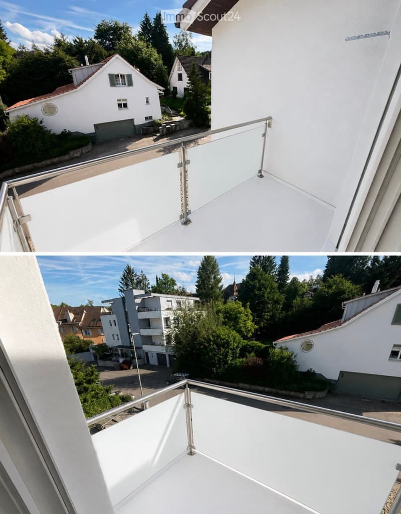 Modern balcony with white railing and glass panels, overlooking a residential area with houses, trees, and a clear blue sky.