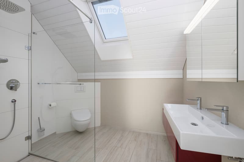 Modern bathroom with a glass-enclosed shower, toilet, double sink, and skylight window. Features white tiles, wooden flooring, and sleek fixtures.