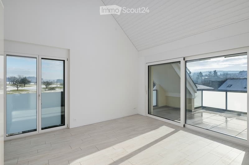 Bright, empty room with large glass sliding doors leading to a balcony, light wooden flooring, and white walls.