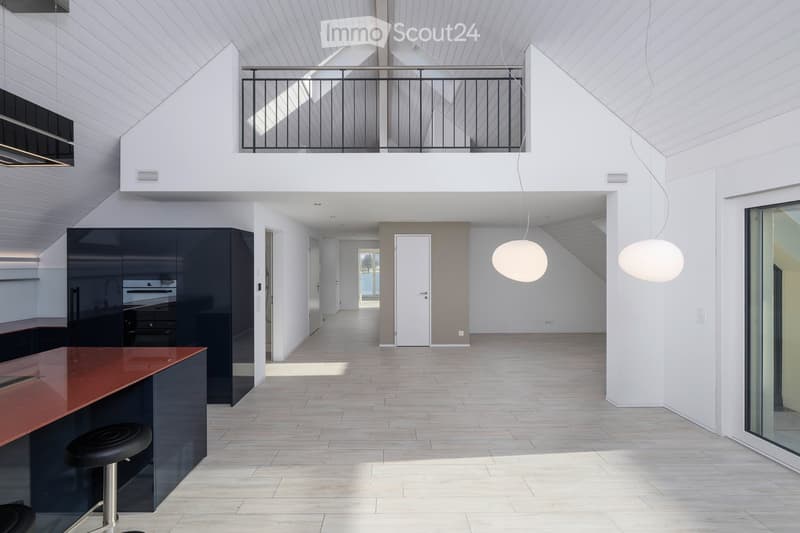 Modern, open-concept kitchen and living area with white walls, wooden flooring, and a raised loft level with a balcony overlooking the space.