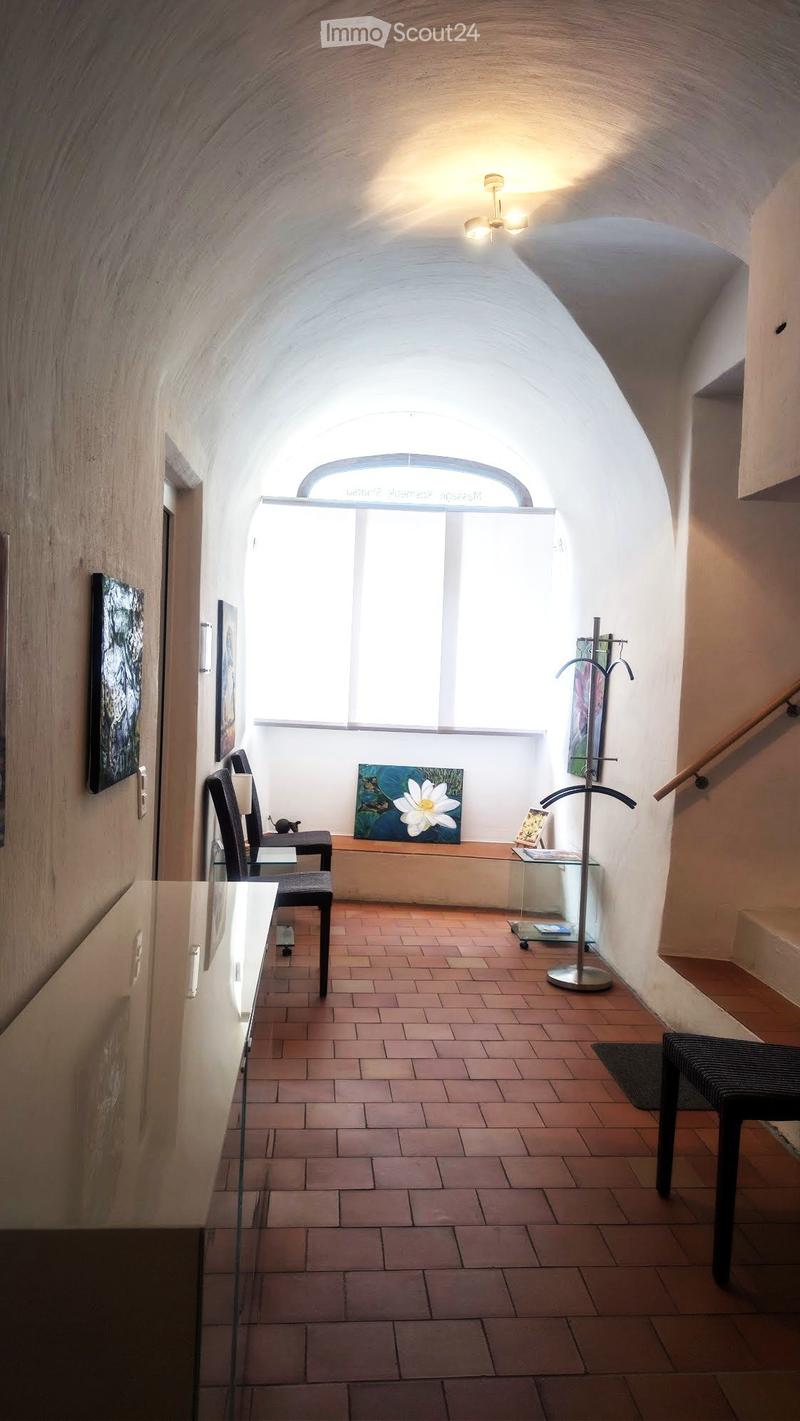 A well-lit hallway with arched ceiling, brick floor, and modern furniture including chairs, a table, and a coat rack.