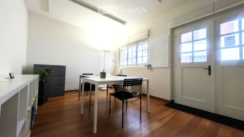 Bright room with wooden flooring, white walls, large windows, a table with chairs, a cabinet, and a potted plant.