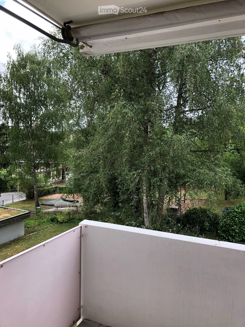 Balcony with white railings, overlooking a green garden area with trees, grass, and outdoor furniture.