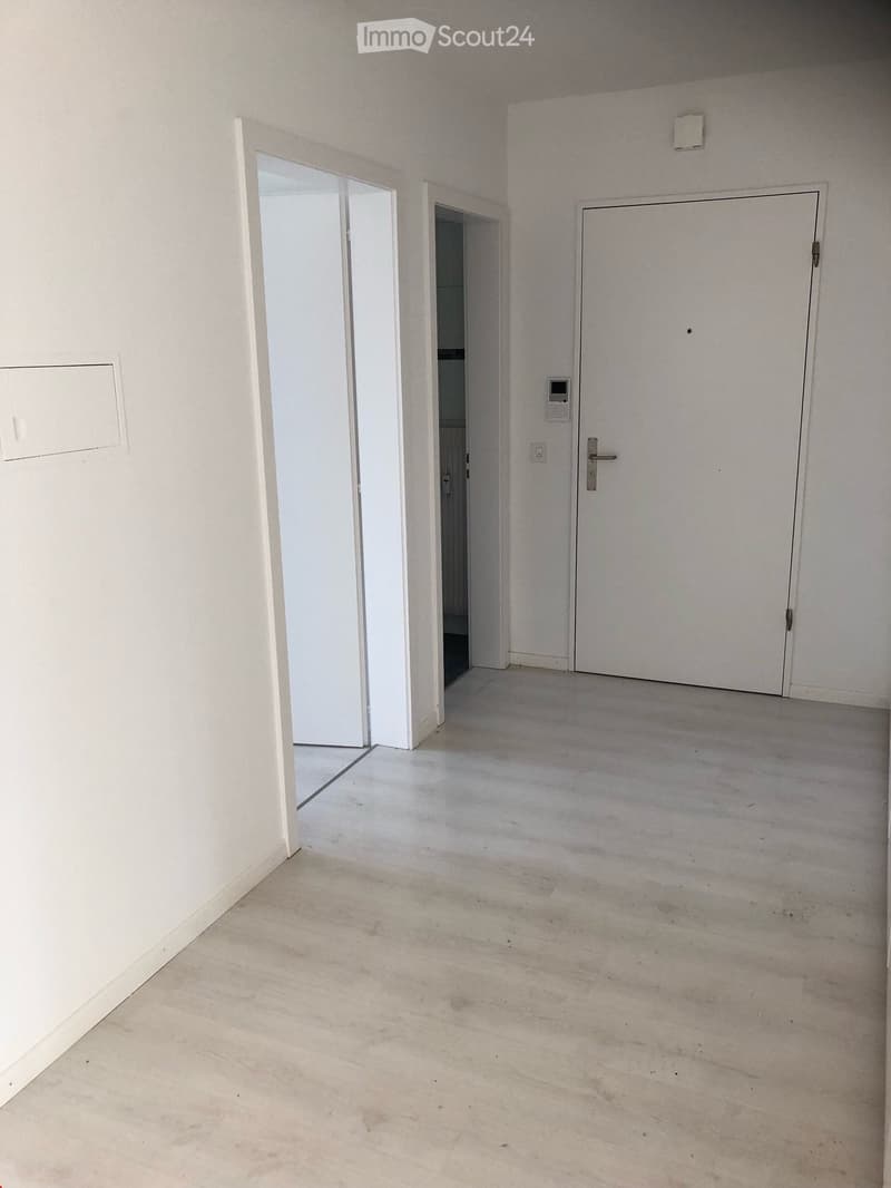 Empty room with white walls, grey concrete floor, and two doors, one leading to another room.