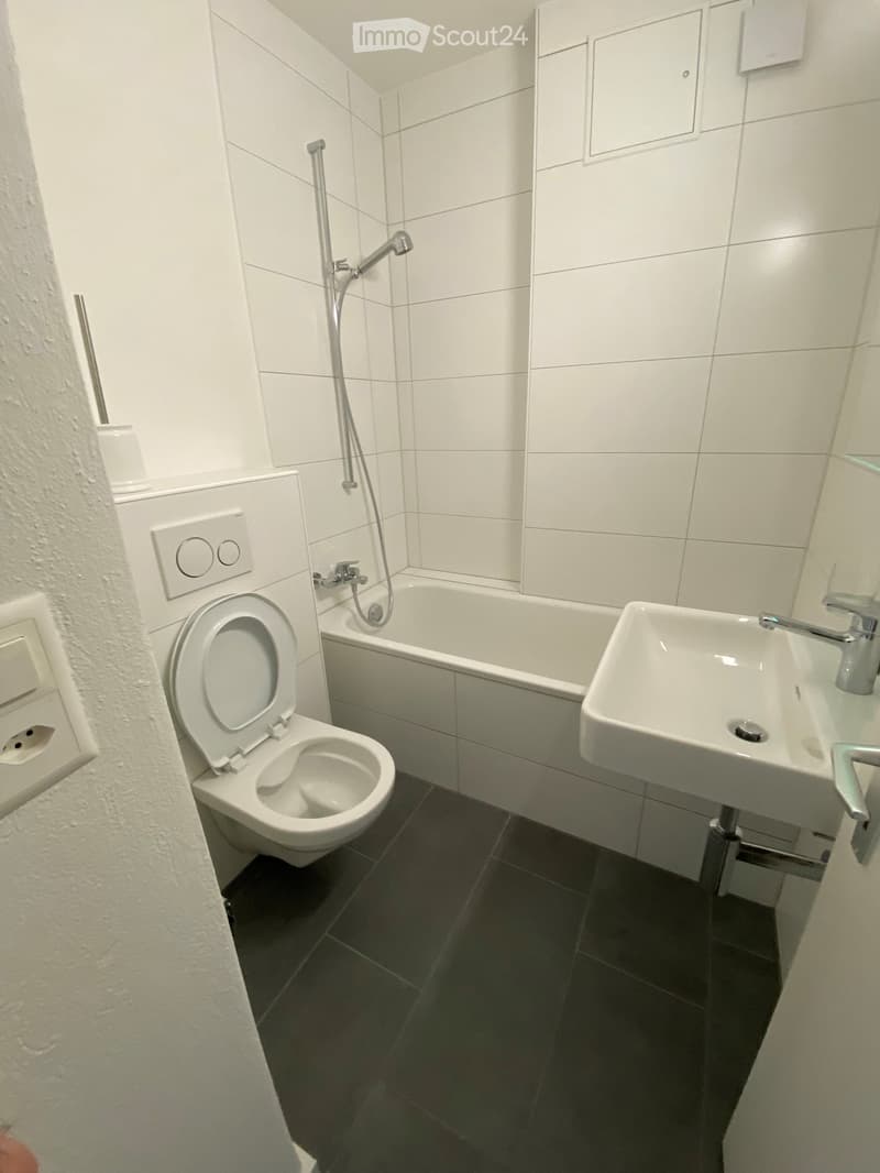 Modern bathroom with white tiles, a toilet, a bathtub, and a sink.