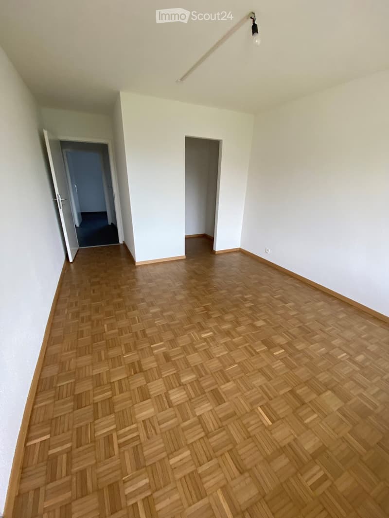 Empty room with wooden herringbone flooring, white walls, and two open doorways leading to other spaces.