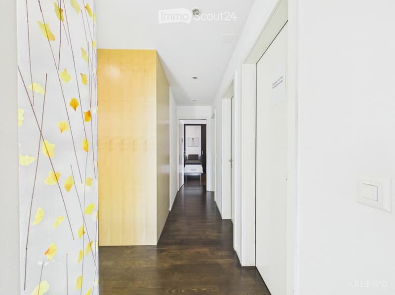 A long, narrow hallway with wooden flooring, white walls, and several closed doors on both sides. A curtain with a yellow leaf pattern is visible on the left side.