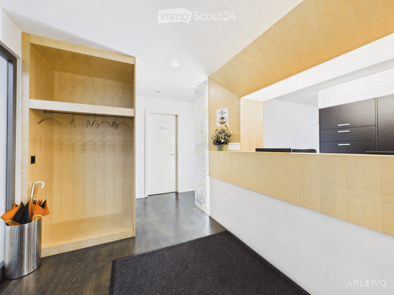 Modern hallway with wooden flooring, built-in wooden storage unit, reception desk, and a small flower arrangement on the counter.