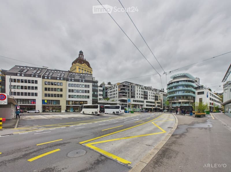 Urban street view with modern and historic buildings, buses, and pedestrians.