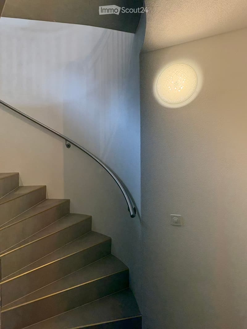 Modern staircase with wooden steps, metal handrail, and a round wall-mounted light fixture.