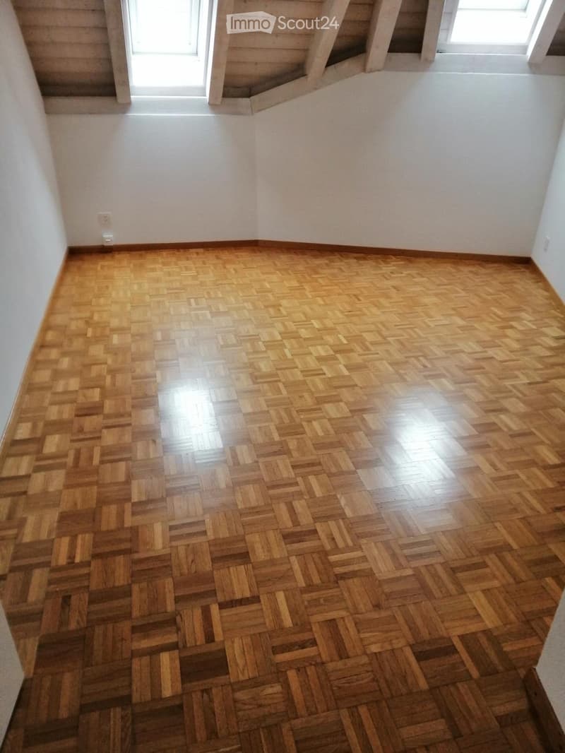 Empty room with polished wooden herringbone flooring and white walls, featuring a window and visible electrical outlet.