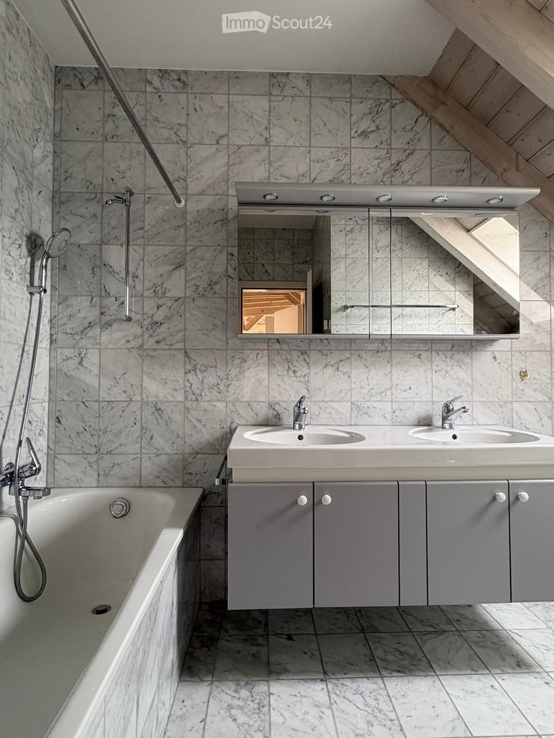 Modern bathroom with marble tiles, a bathtub, double sink, and mirrored cabinet.