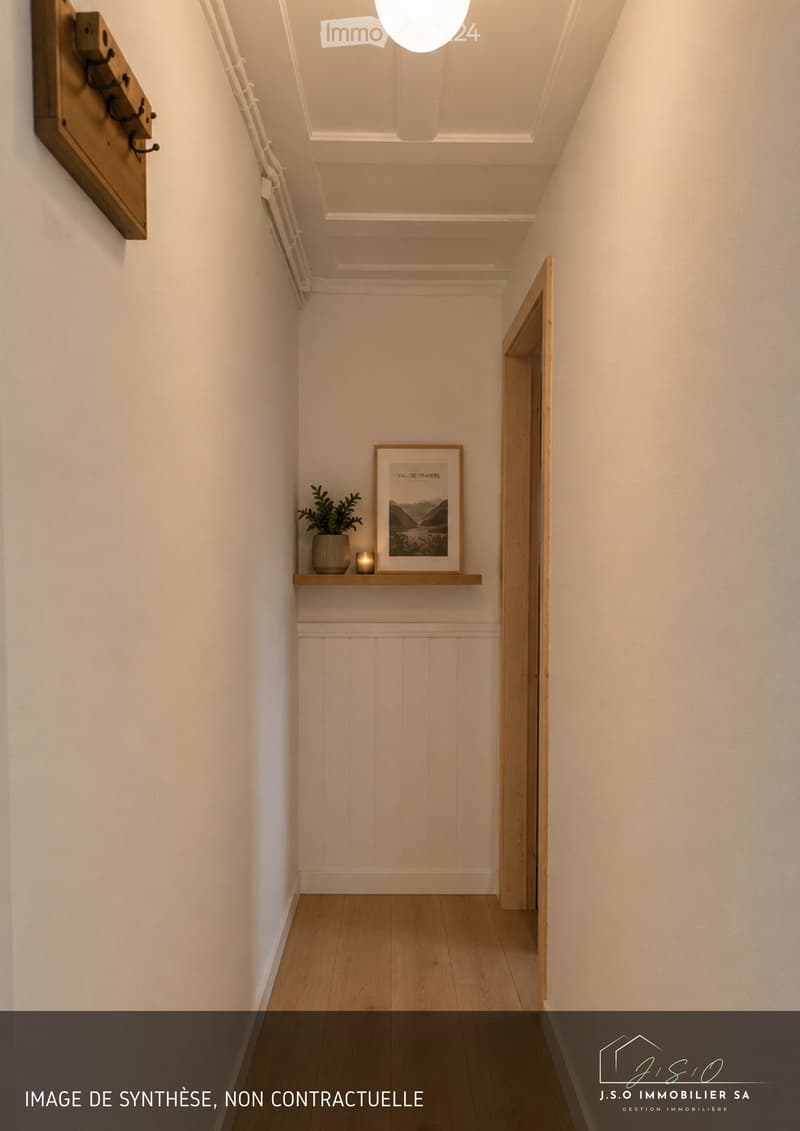 A narrow hallway with light wooden flooring, white walls, and a small shelf with a plant and framed picture. The ceiling has recessed lighting and a decorative molding.
