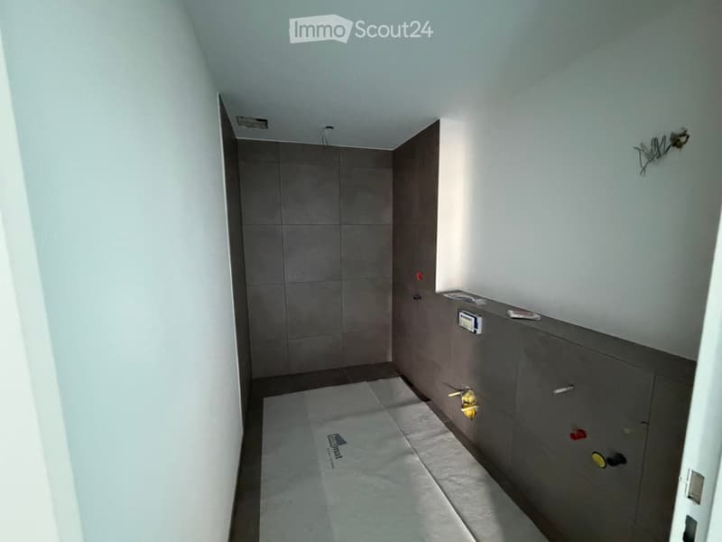 Empty hallway with grey tiled walls, white ceiling, and a white floor mat in the center.
