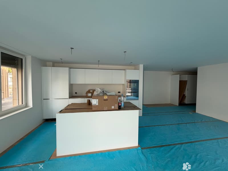 Empty kitchen with white cabinets, a countertop, and a window. The floor is covered with a blue protective sheet.