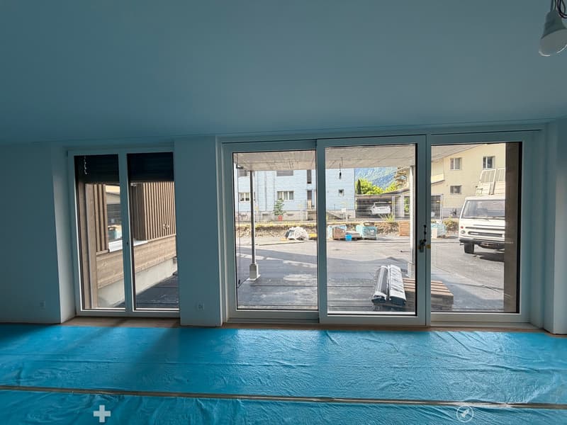 Empty room with light blue walls, large sliding glass doors leading to an outdoor area, and a blue protective sheet covering the floor.